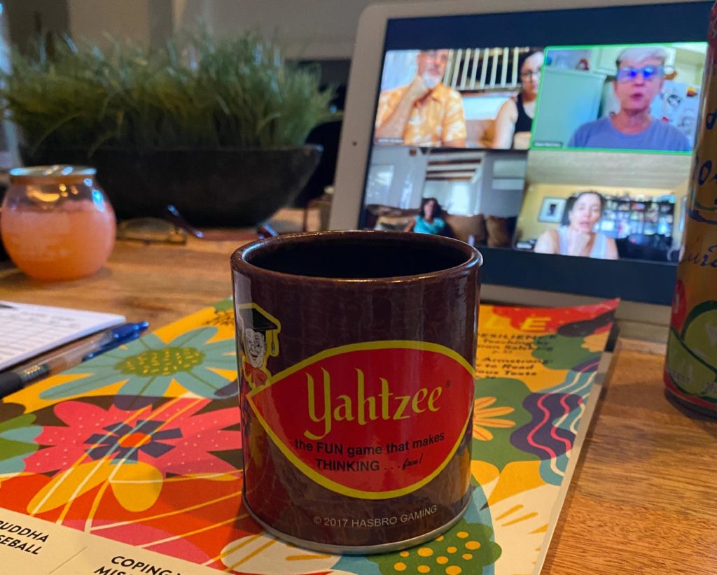 A Yahtzee-branded coffee cup with a tabled in the background, showing an ongoing video call.